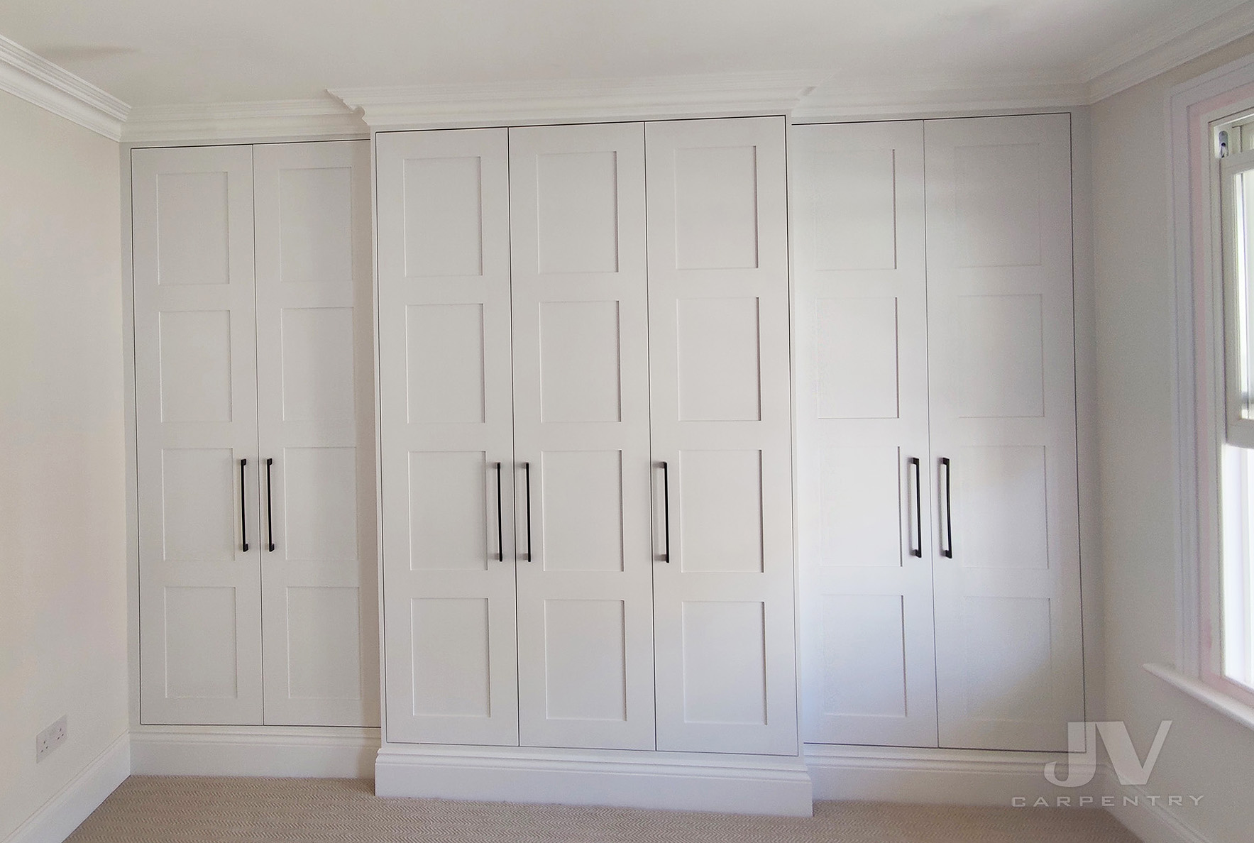 Fitted wardrobe around chimney breast in London with deep alcove storage and shaker doors.